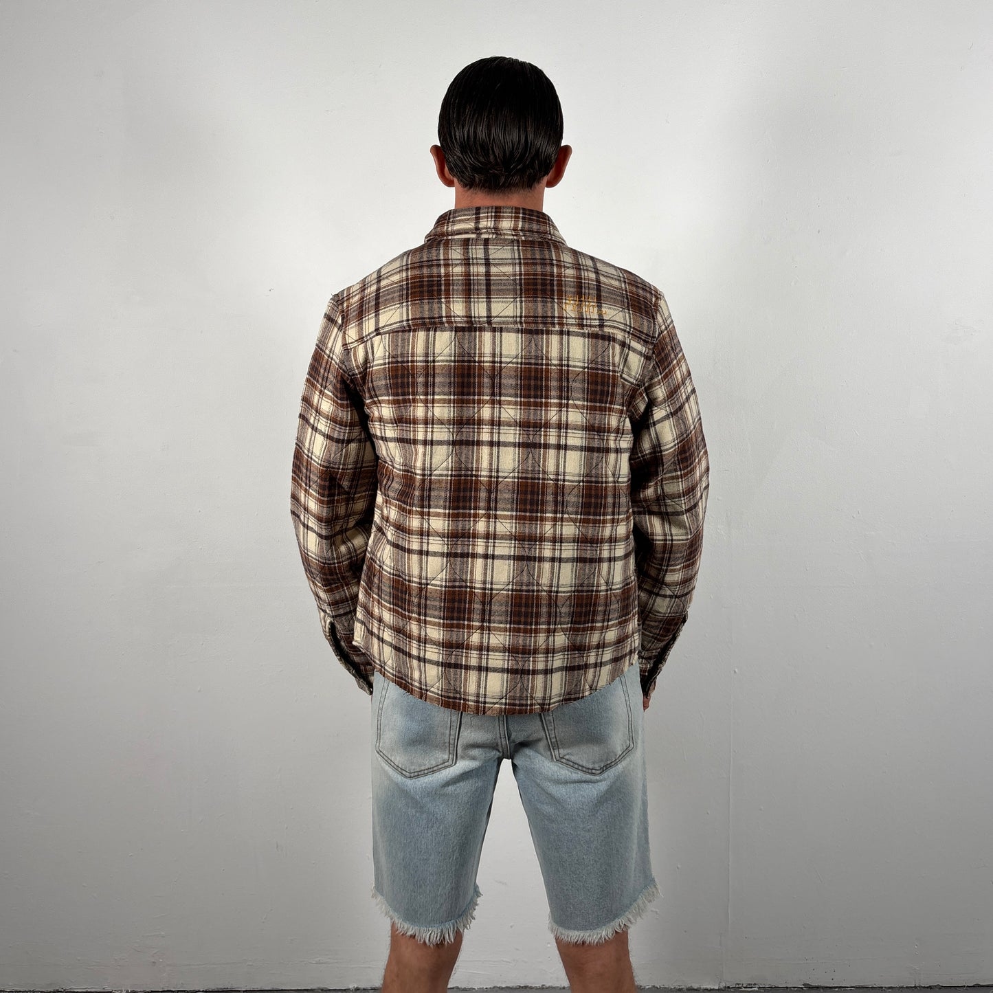 Person wearing a plaid shirt and denim shorts against a plain background