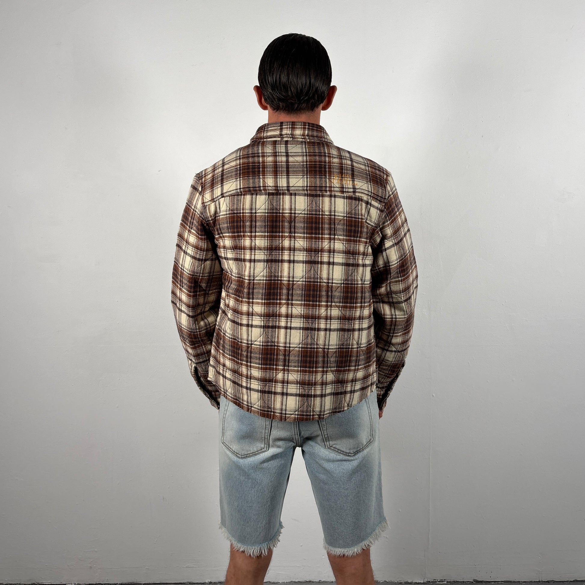 Person wearing a plaid shirt and denim shorts against a plain background