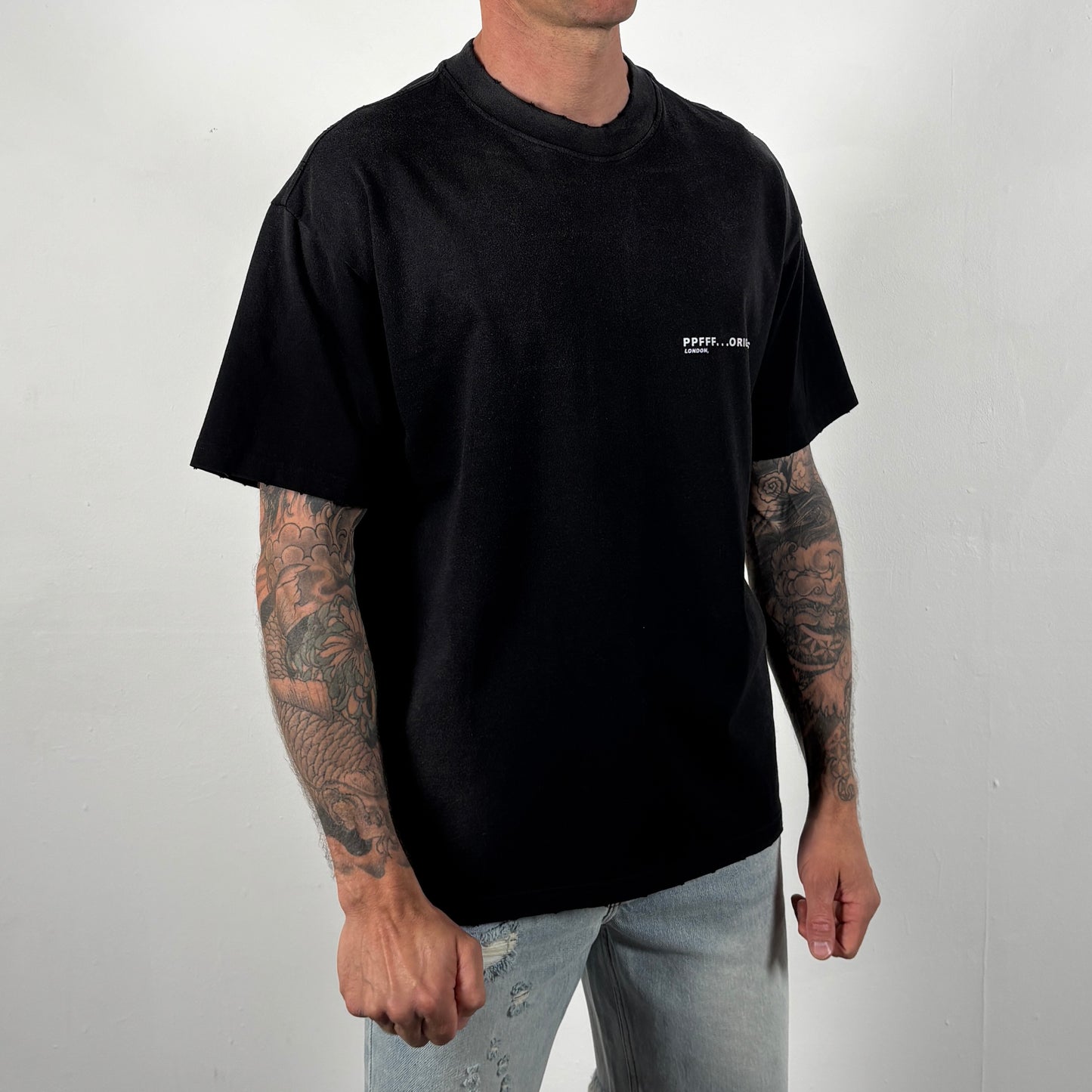 Person wearing a black t-shirt with a small white logo on a plain background