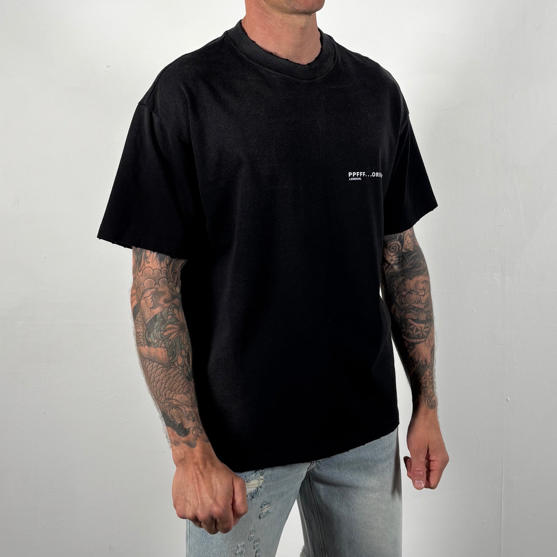 Person wearing a black t-shirt with a small white logo on a plain background