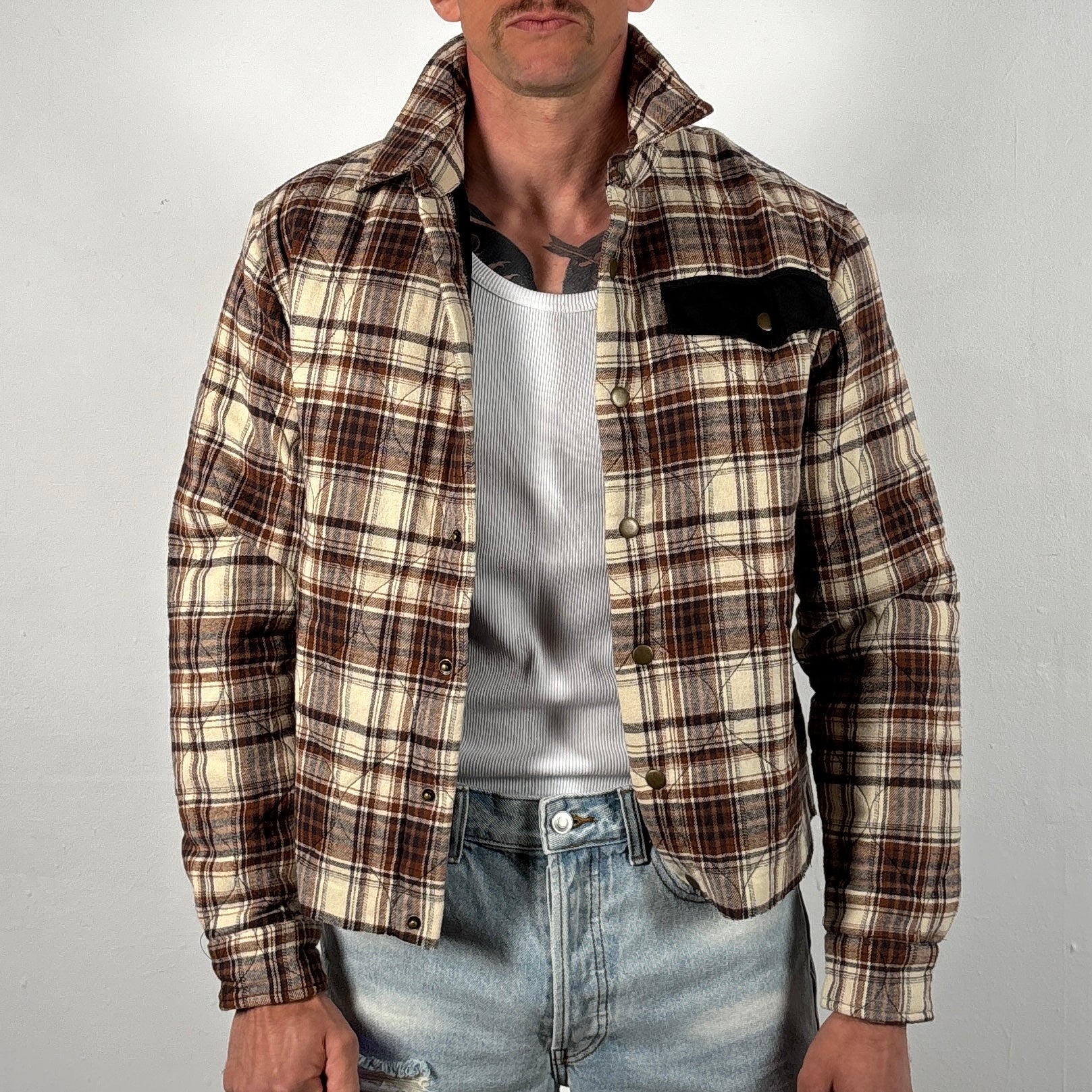 Man wearing a plaid shirt over a gray t-shirt with a plain background
