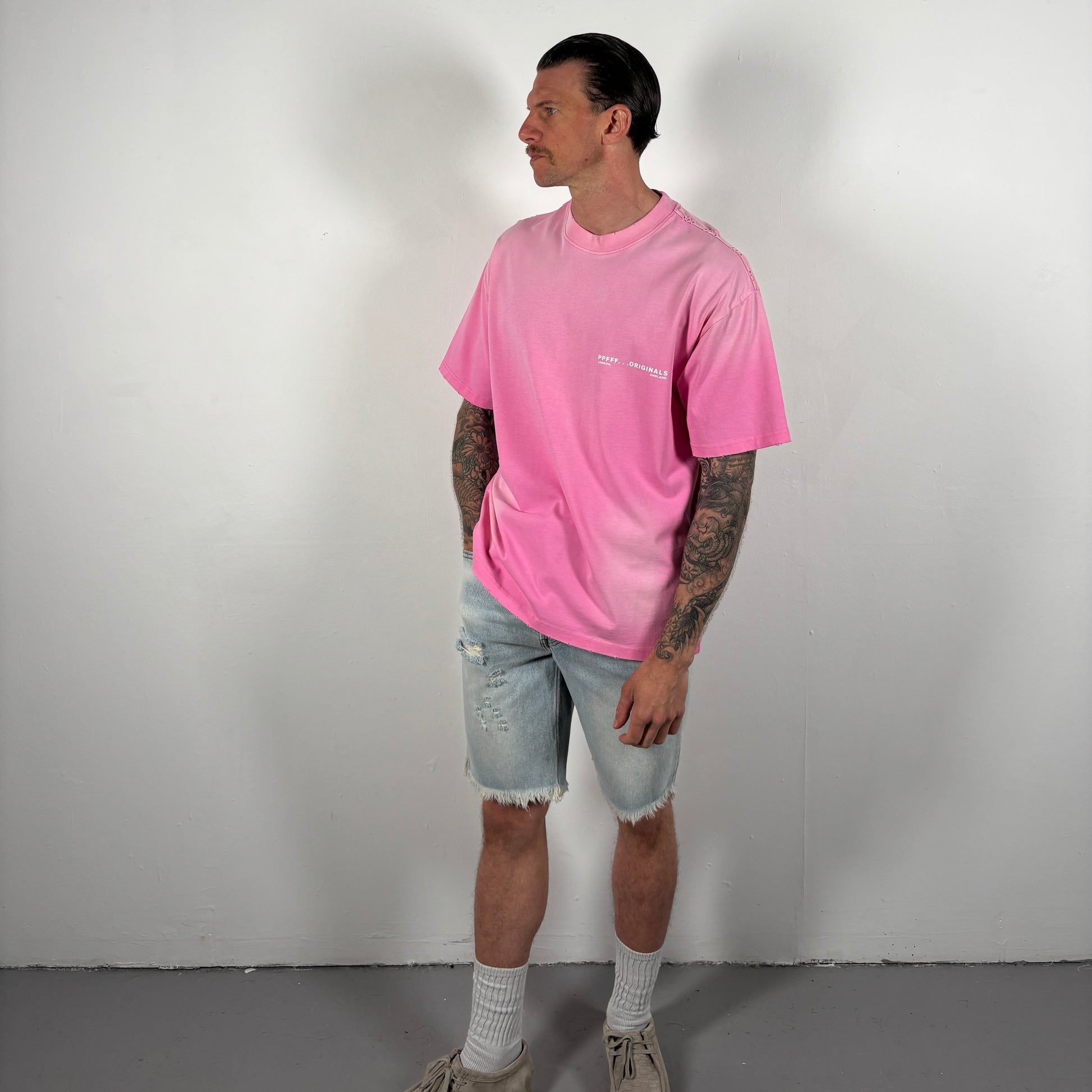 Person wearing a pink t-shirt and light blue shorts against a plain background